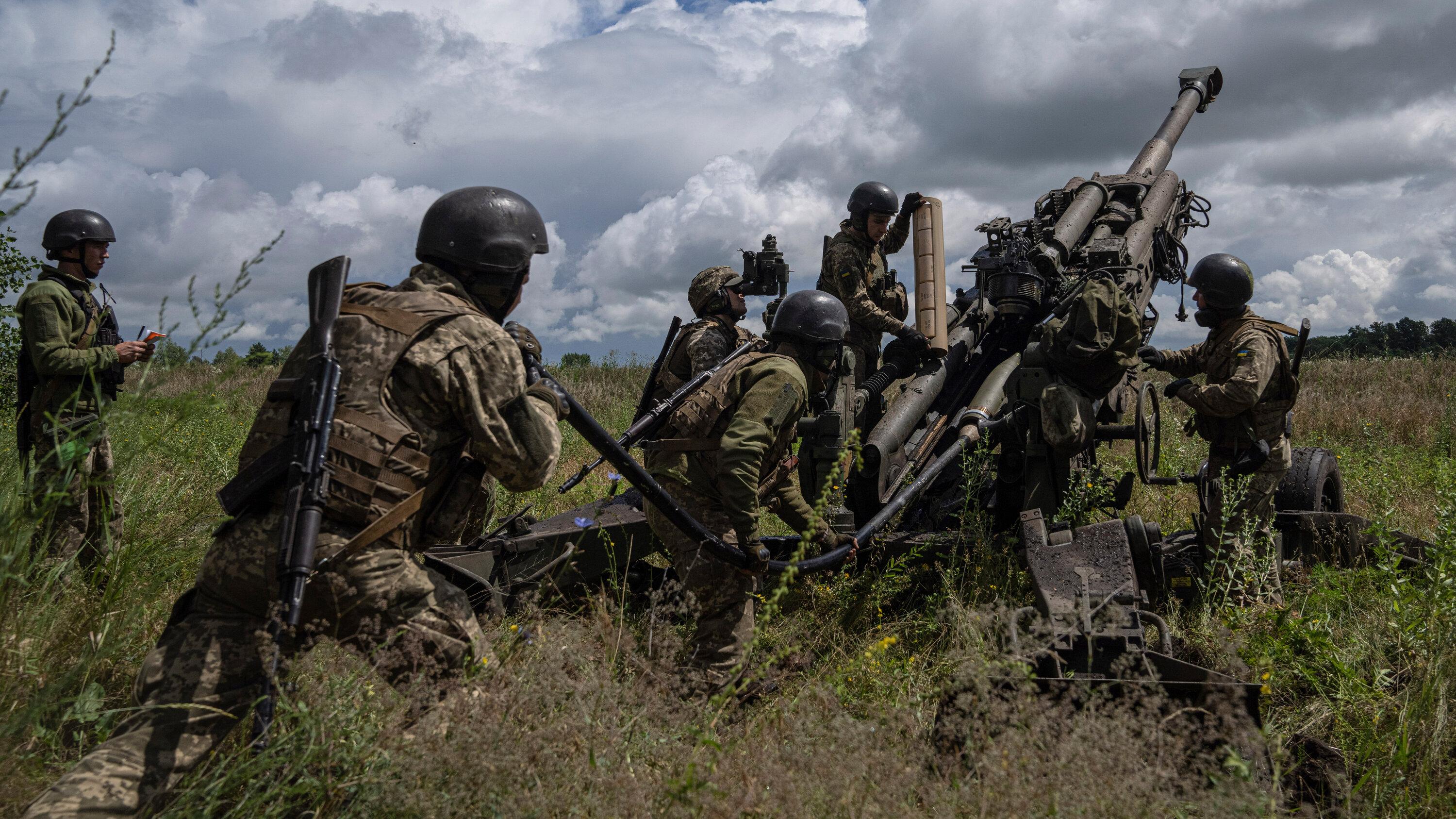 Ukrainian soldiers are operating artillery in a grassy area under a partly cloudy sky, showcasing their military capabilities amid NATO's support.